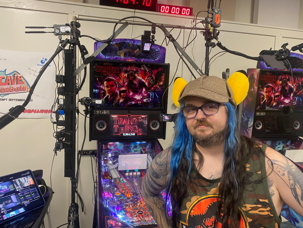 Stranger Things pinball machine with colorful display and person wearing yellow ear muffs