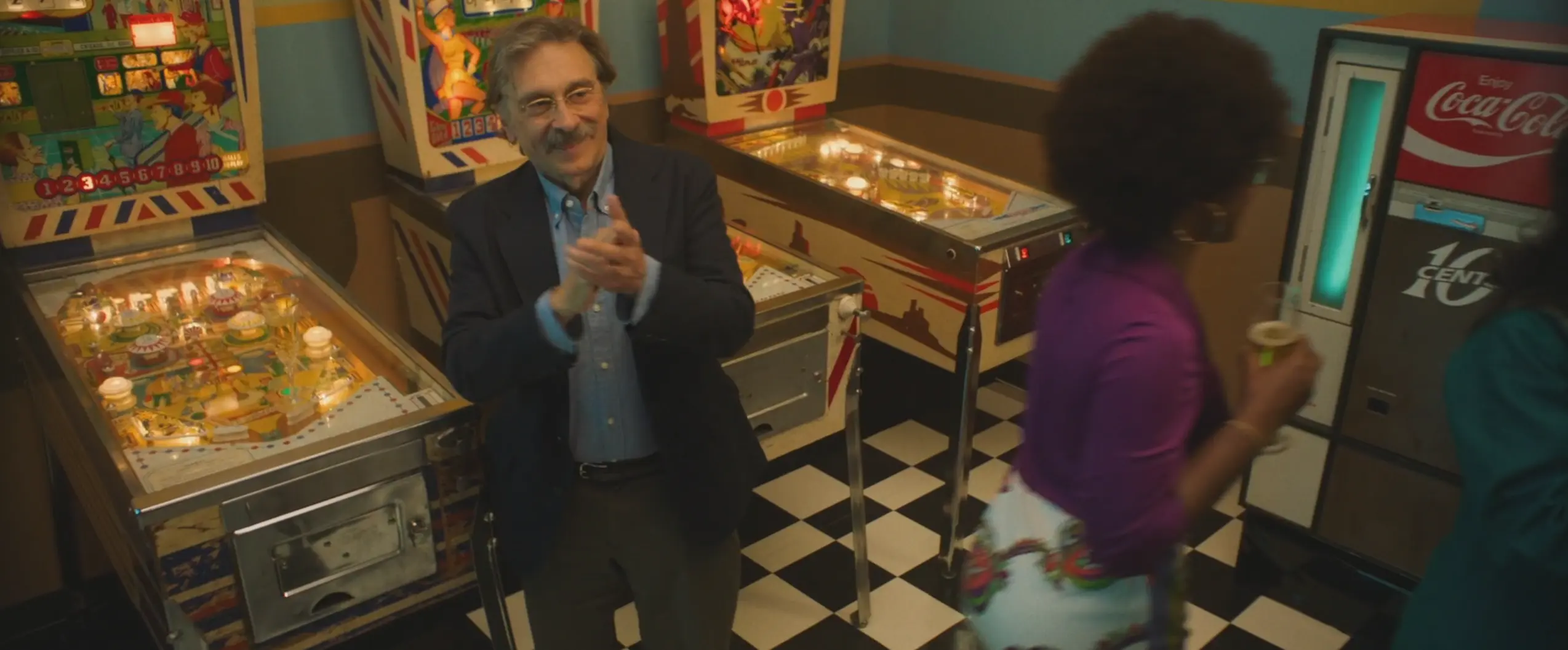 Man explaining pinball machines in retro arcade with checkered floor